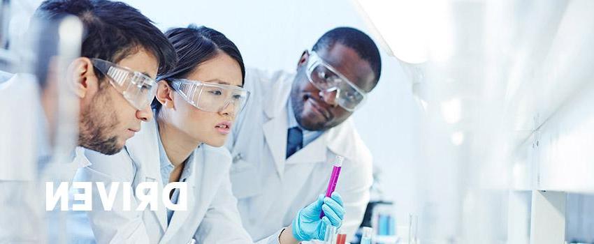 Driven text over an image of three people working in a lab with safety glasses and white coats on,